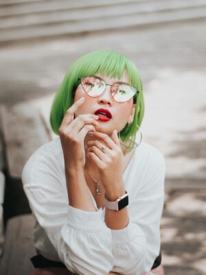 Portrait of a stylish woman with green hair and sunglasses posing outdoors.
